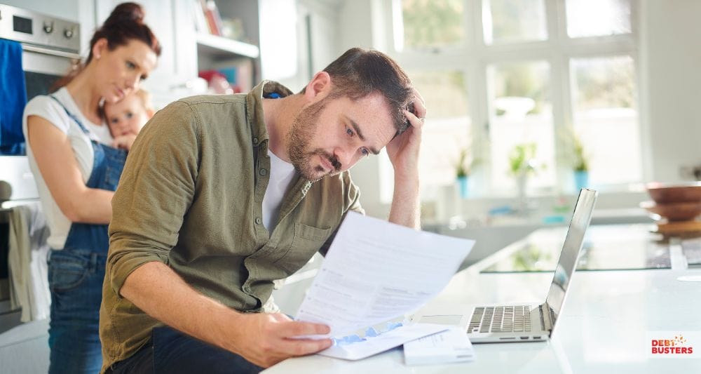 Stressed man reviews bills for bankruptcy means test while family watches in background