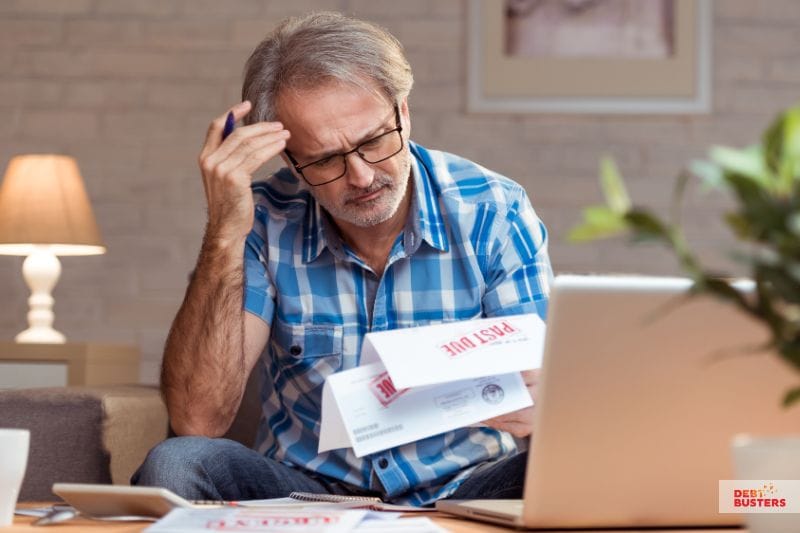 Stressed man reviewing overdue bills showing impact of bankruptcy vs insolvency